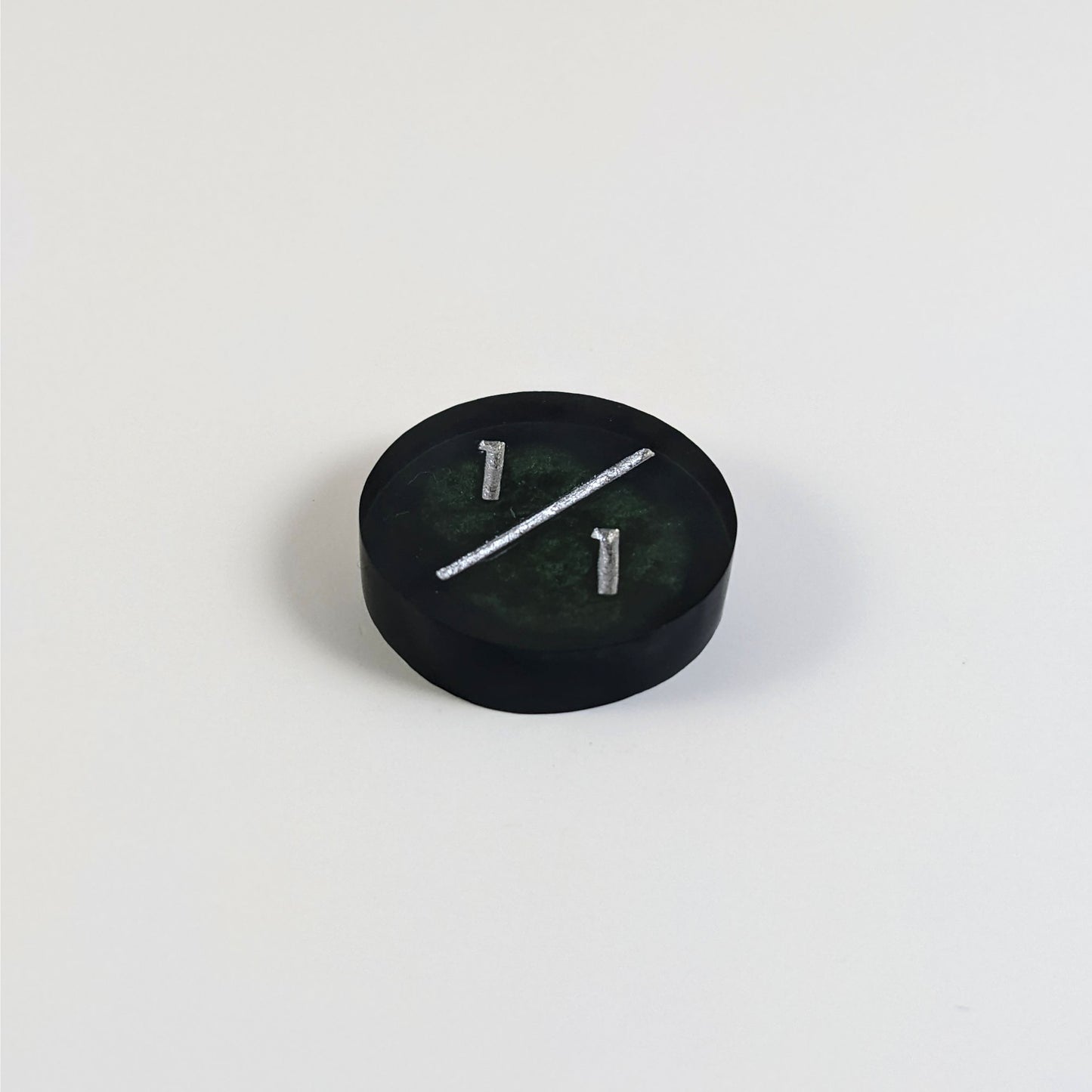 A low angle photo of a black and green 1/1 token with silver numbers sits on a white background.