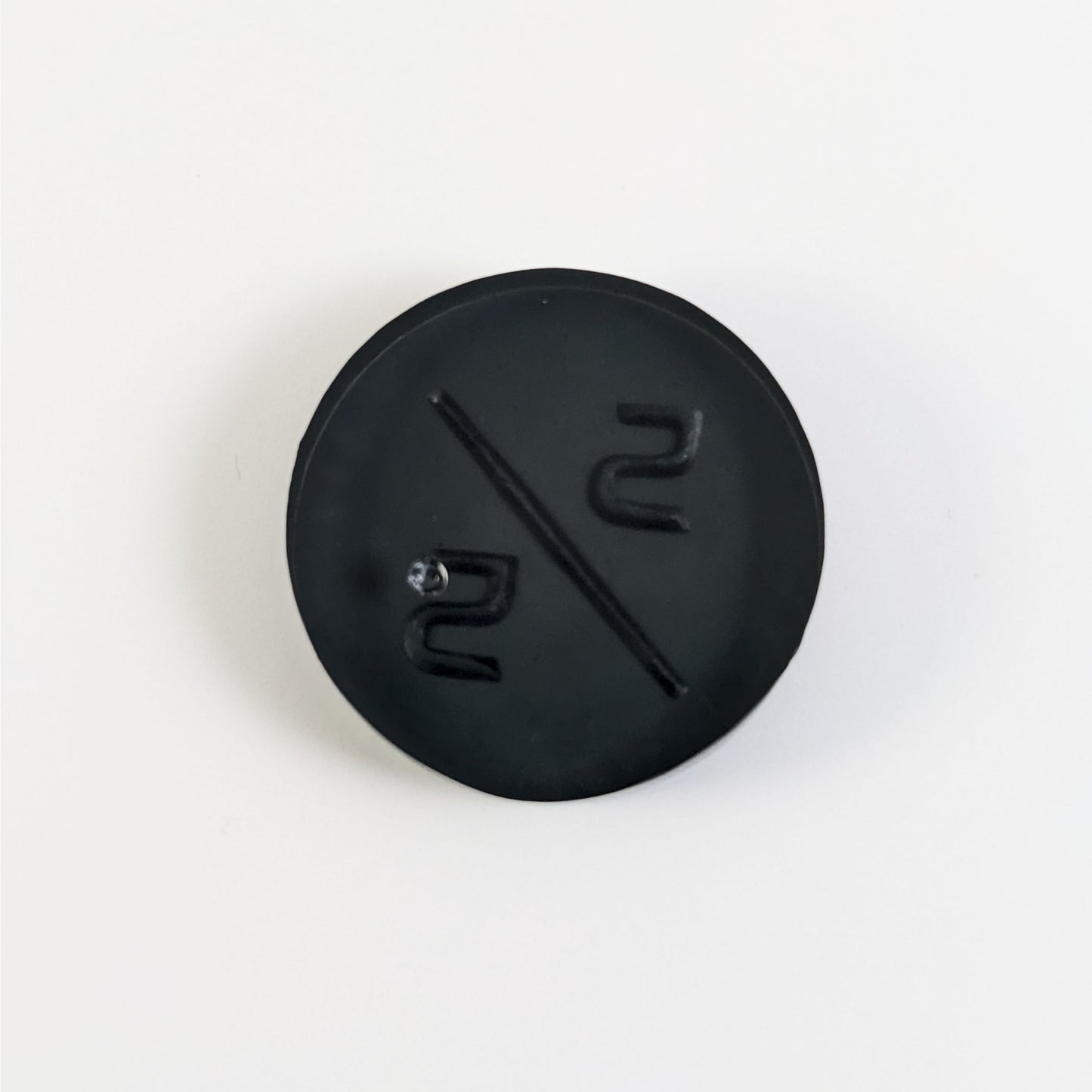 A top down photo of the back of a black 5/5 token with silver numbers sitting on a white background. A bubble is visible.