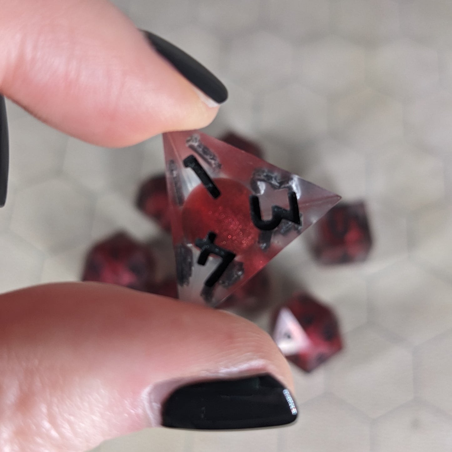 The d4 die is being held up to the camera to show off the red, spherical insert and the dark glow the black numbers give in the clear shell. The face with 1, 3, and 4 in the corners is angled toward the camera.