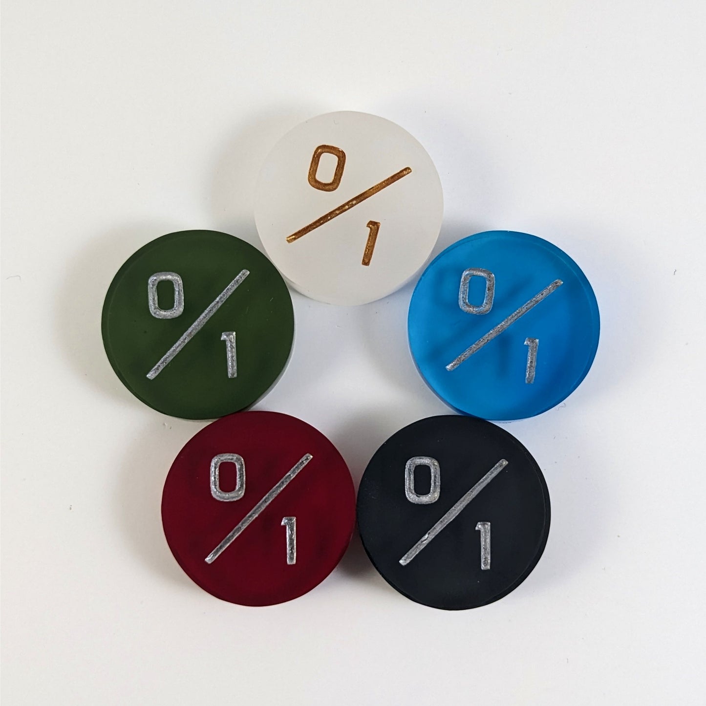 Five 0/1 tokens arranged in a circle face up. White with gold numbers is at the top and blue, black, red, and dark green all with silver numbers follow going clockwise.
