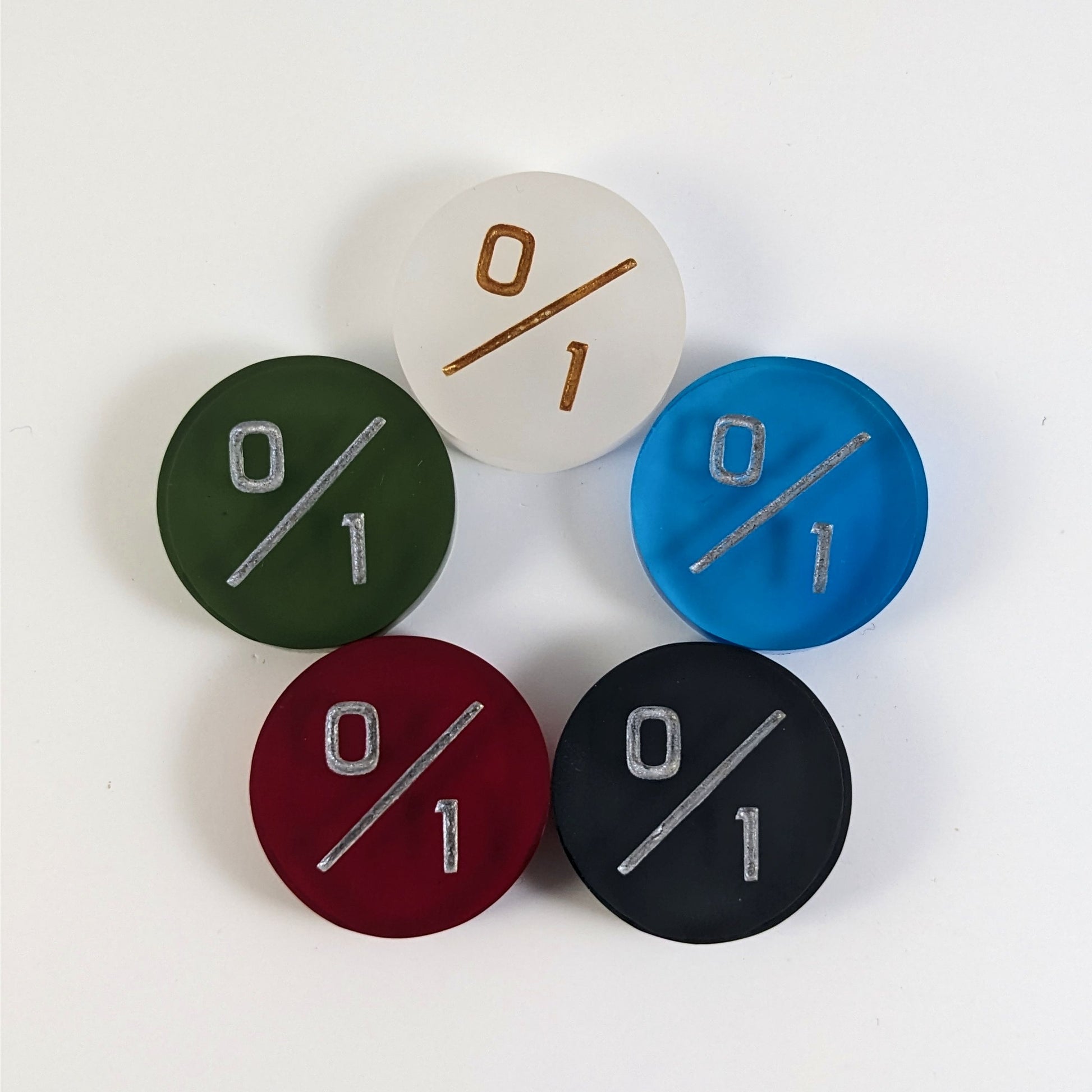 Five 0/1 tokens arranged in a circle face up. White with gold numbers is at the top and blue, black, red, and dark green all with silver numbers follow going clockwise.