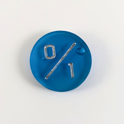 A top down photo of a blue 0/1 token with silver numbers sits on a white background. A bubble is visible near the 0 and another towards the right side but they are on the back side of the token.