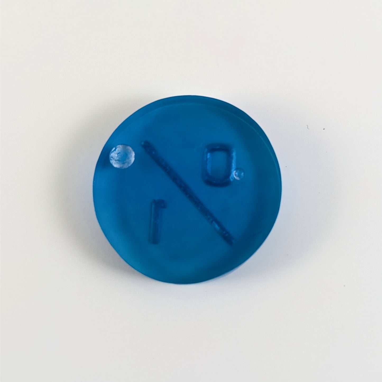A top down photo of the back of a blue 0/1 token with silver numbers sitting on a white background. Two bubbles are visible.