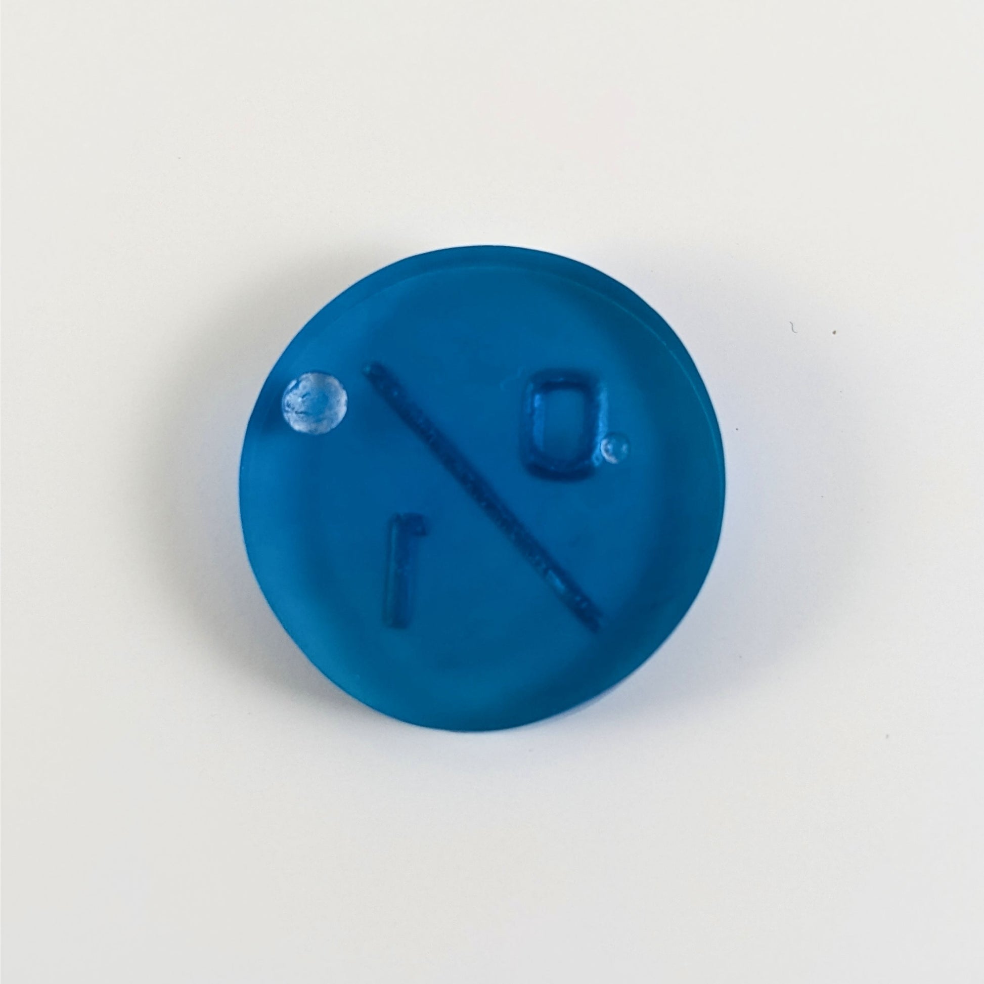 A top down photo of the back of a blue 0/1 token with silver numbers sitting on a white background. Two bubbles are visible.