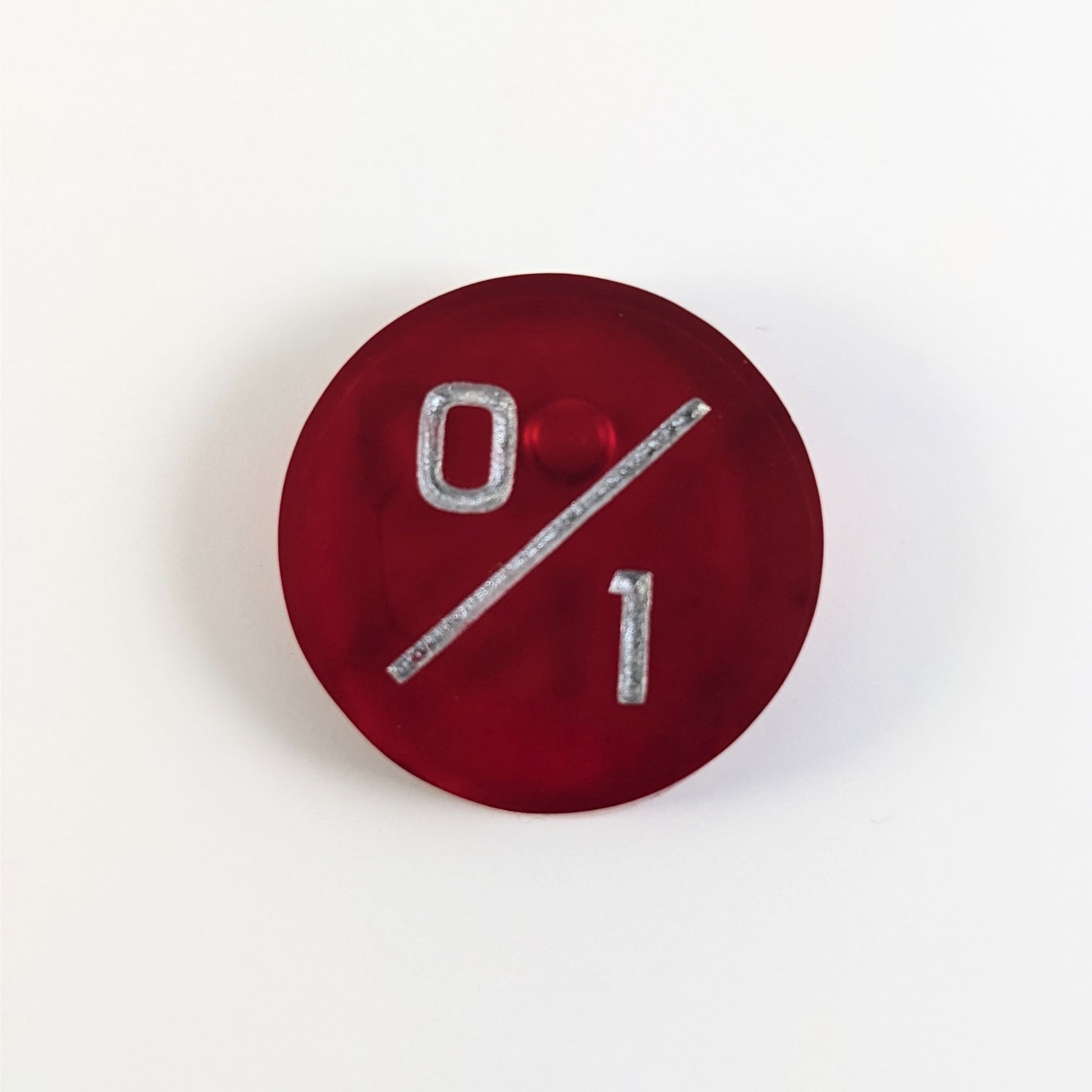 A top down photo of a red 0/1 token with silver numbers sits on a white background. A bubble is visible near the 0 but it is on the back side of the token.