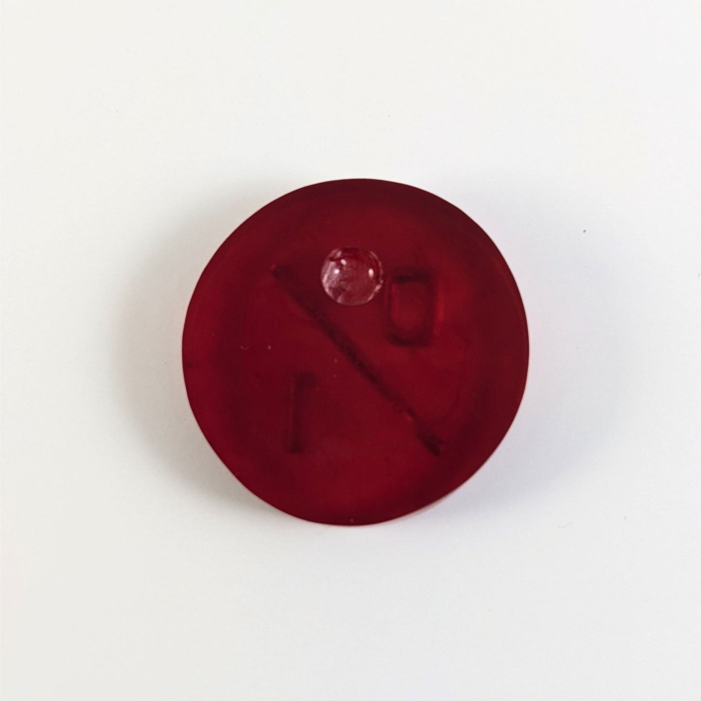 A top down photo of the back of a red 0/1 token with silver numbers sitting on a white background. A bubble is visible.