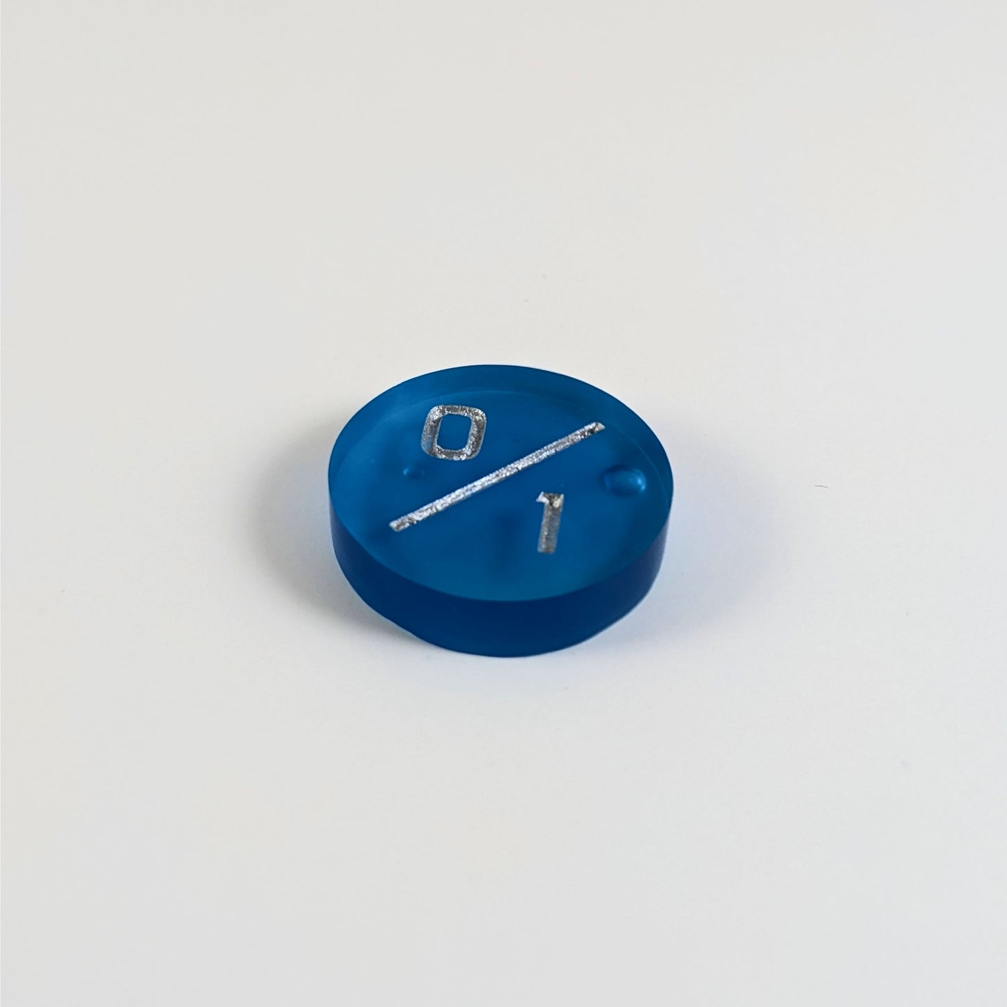 A low angle photo of a blue 0/1 token with silver numbers sits on a white background. There are bubbles visible towards the right side and just under the 0, but they are clearly on the back of the token.