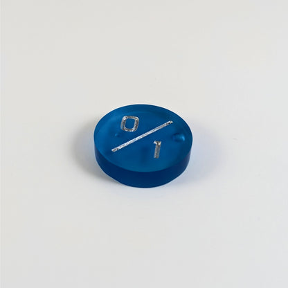 A low angle photo of a blue 0/1 token with silver numbers sits on a white background. There are bubbles visible towards the right side and just under the 0, but they are clearly on the back of the token.