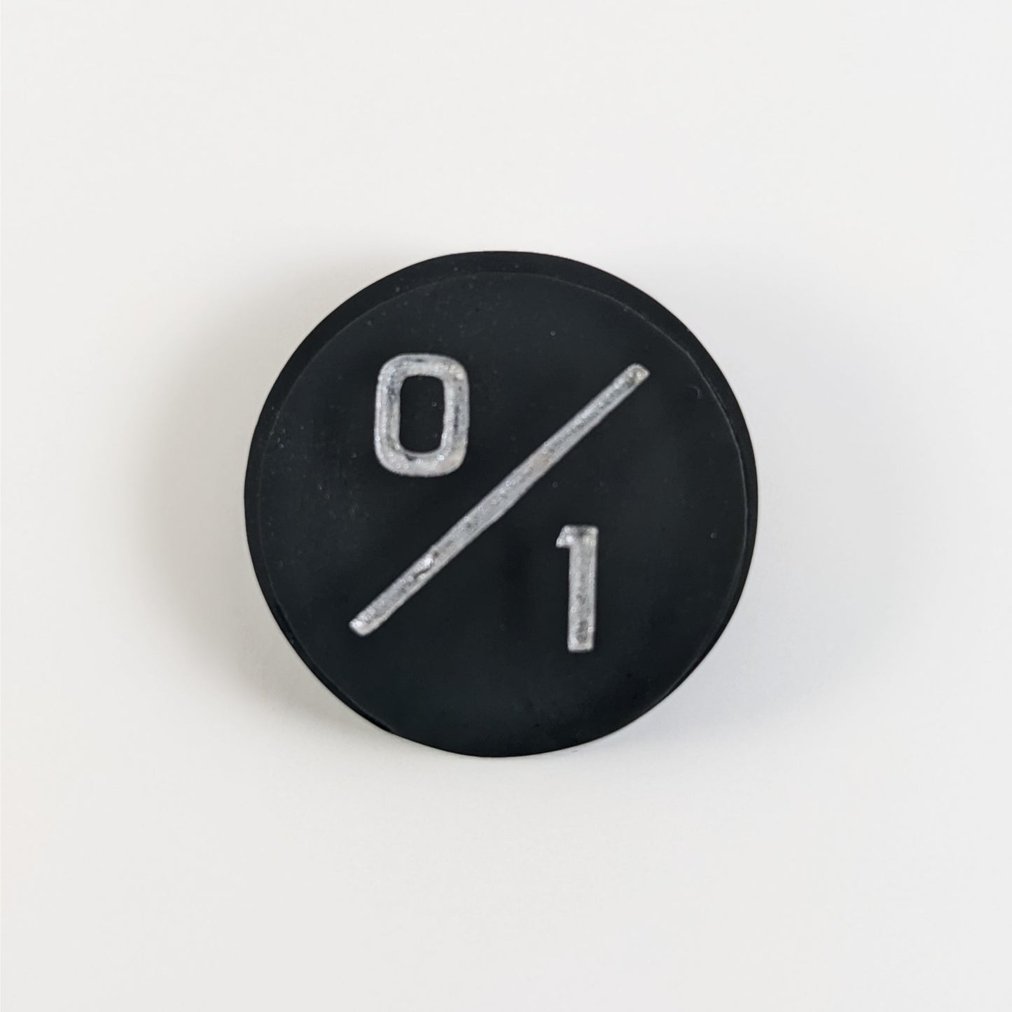 A top down photo of a black 0/1 token with silver numbers sits on a white background.
