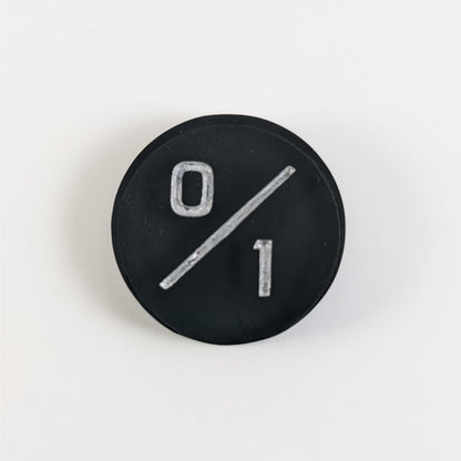 A top down photo of a black 0/1 token with silver numbers sits on a white background.
