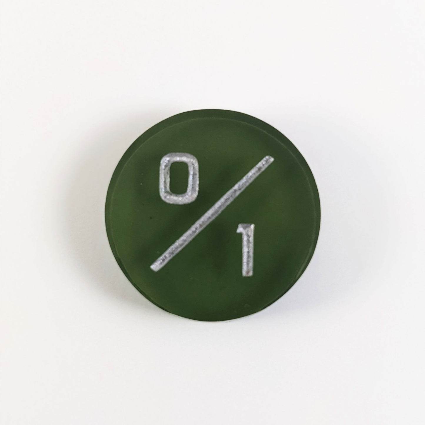 A top down photo of a dark green 0/1 token with silver numbers sits on a white background.