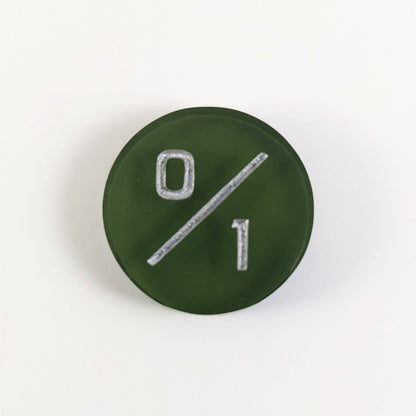 A top down photo of a dark green 0/1 token with silver numbers sits on a white background.