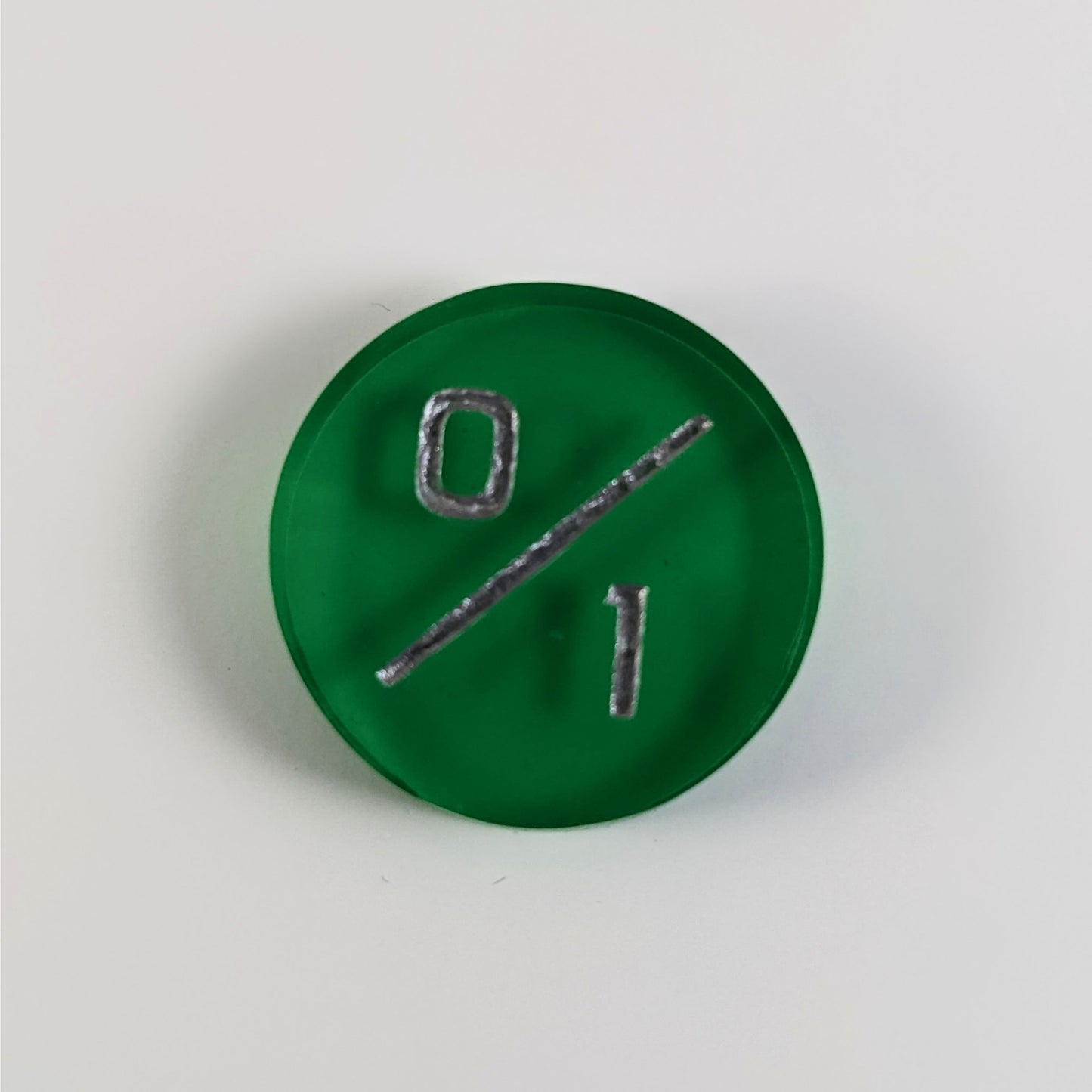 A top down photo of a green 0/1 token with silver numbers sits on a white background.