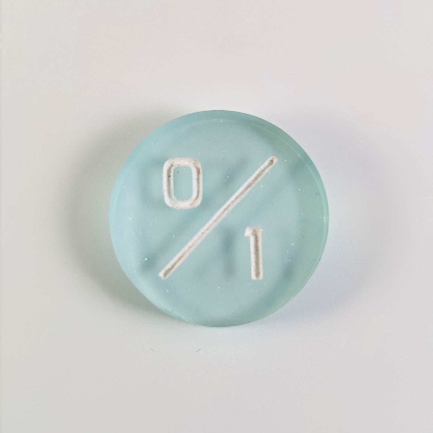 A top down photo of a frosty white and blue 0/1 token with white numbers sits on a white background.