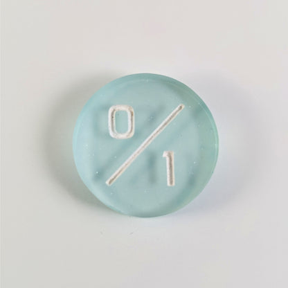 A top down photo of a frosty white and blue 0/1 token with white numbers sits on a white background.