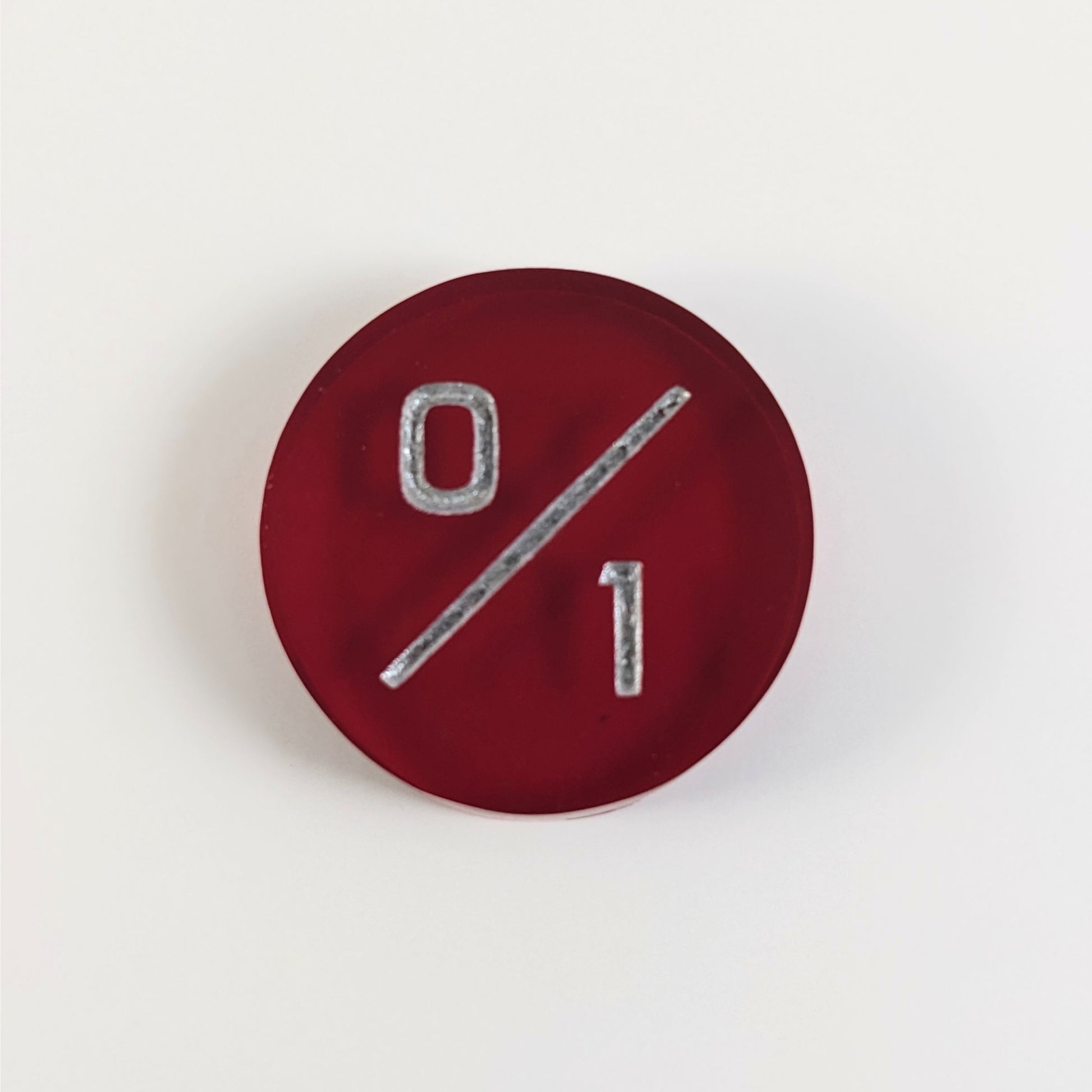 A top down photo of a red 0/1 token with silver numbers sits on a white background.