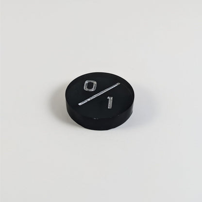A low angle photo of a black 0/1 token with silver numbers sits on a white background.