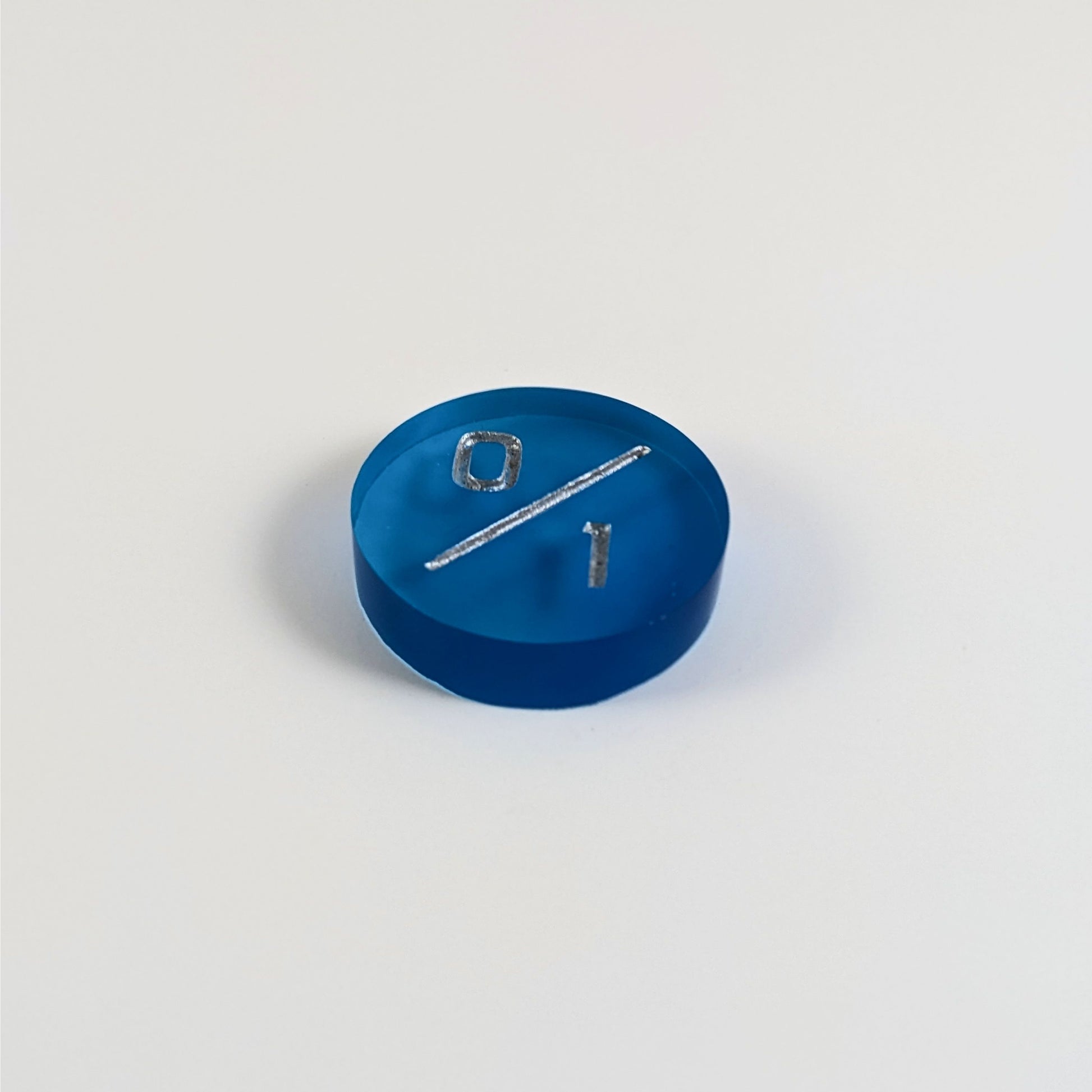 A low angle photo of a blue 0/1 token with silver numbers sits on a white background.
