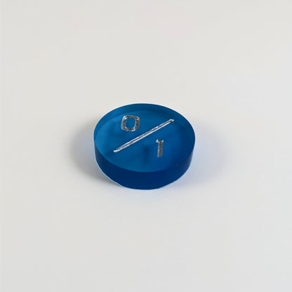 A low angle photo of a blue 0/1 token with silver numbers sits on a white background.