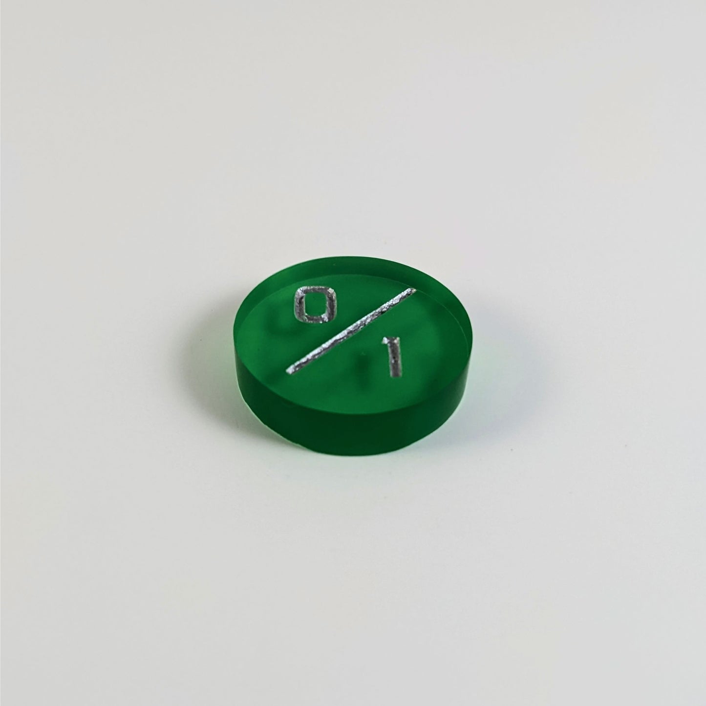 A low angle photo of a green 0/1 token with silver numbers sits on a white background.