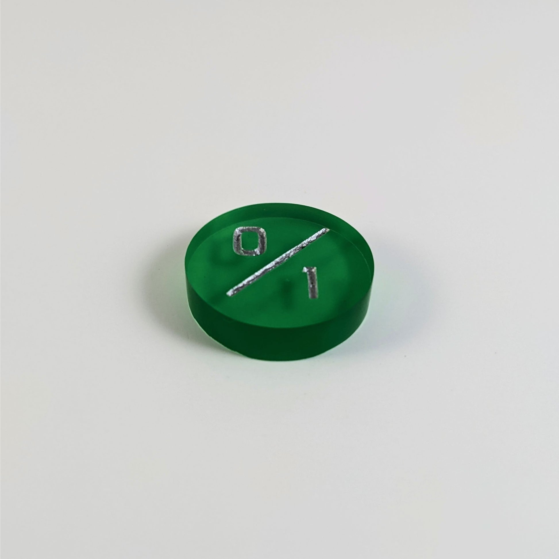 A low angle photo of a green 0/1 token with silver numbers sits on a white background.