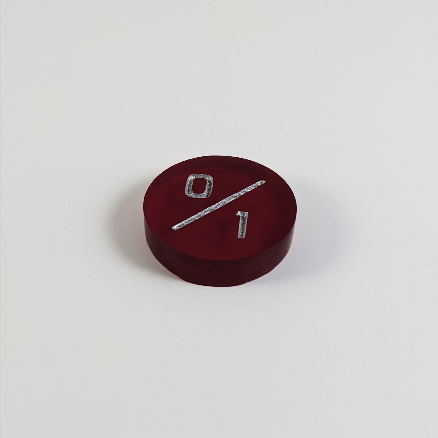 A low angle photo of a red 0/1 token with silver numbers sits on a white background.