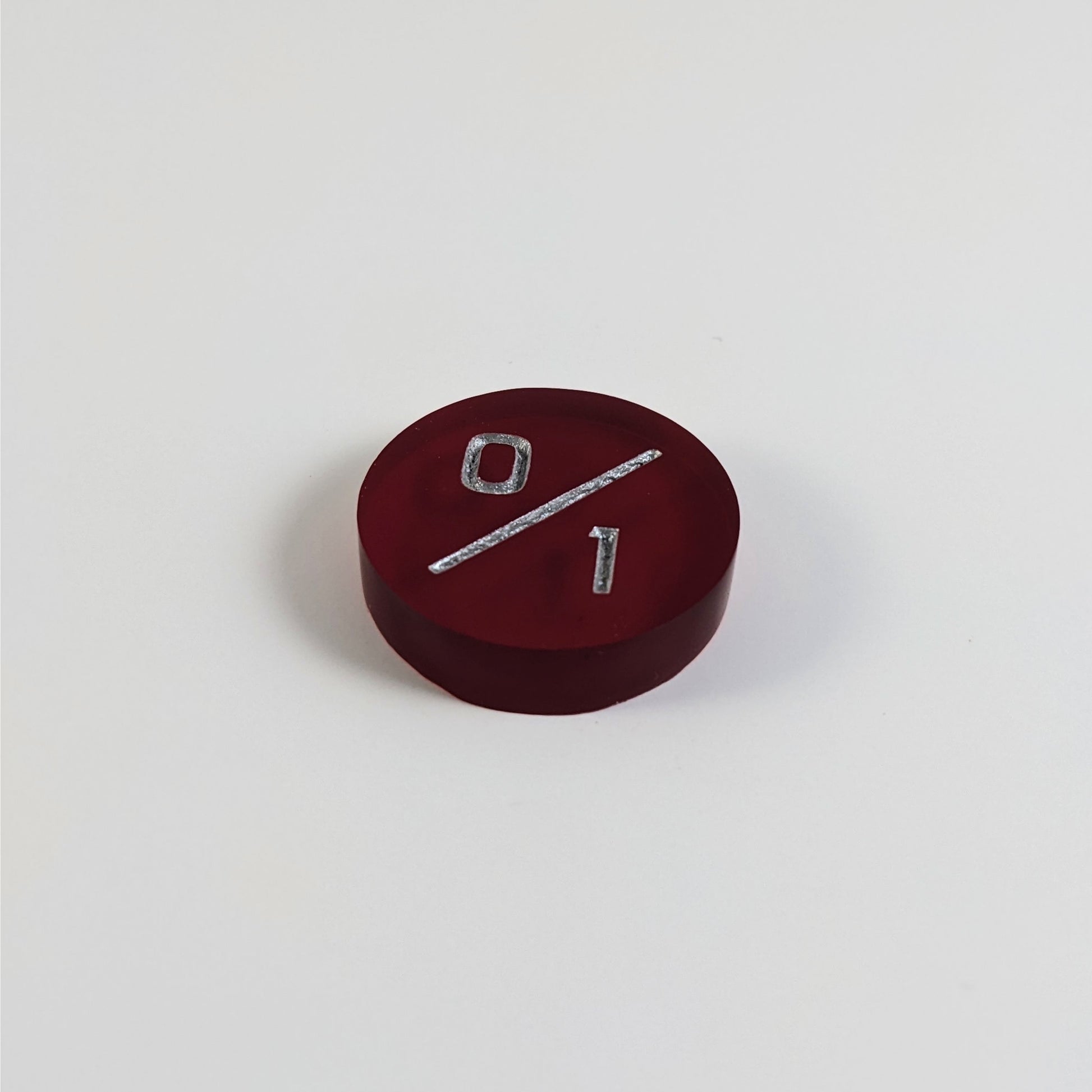 A low angle photo of a red 0/1 token with silver numbers sits on a white background.
