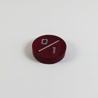 A low angle photo of a red 0/1 token with silver numbers sits on a white background.