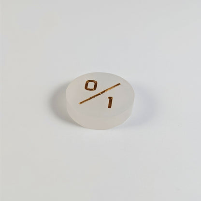 A low angle photo of a white 0/1 token with gold numbers sits on a white background.