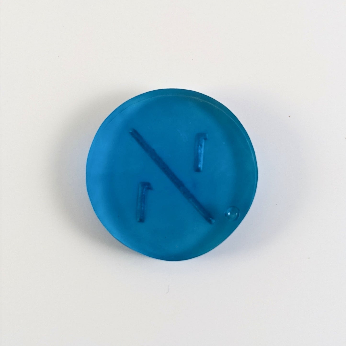 A top down photo of the back of a blue 1/1 token with silver numbers sitting on a white background. A bubble is visible.