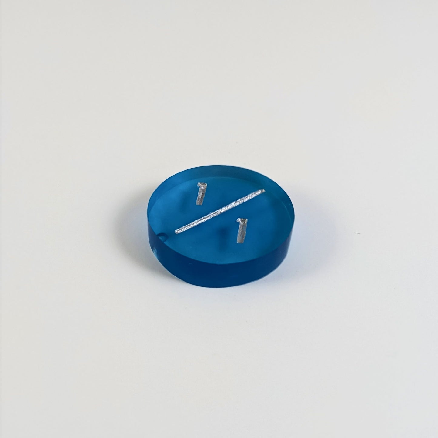 A low angle photo of a blue 1/1 token with silver numbers sits on a white background. The bubble is visible at the bottom end of the slash and is on the back of the token.