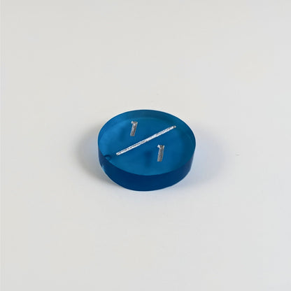 A low angle photo of a blue 1/1 token with silver numbers sits on a white background. The bubble is visible at the bottom end of the slash and is on the back of the token.