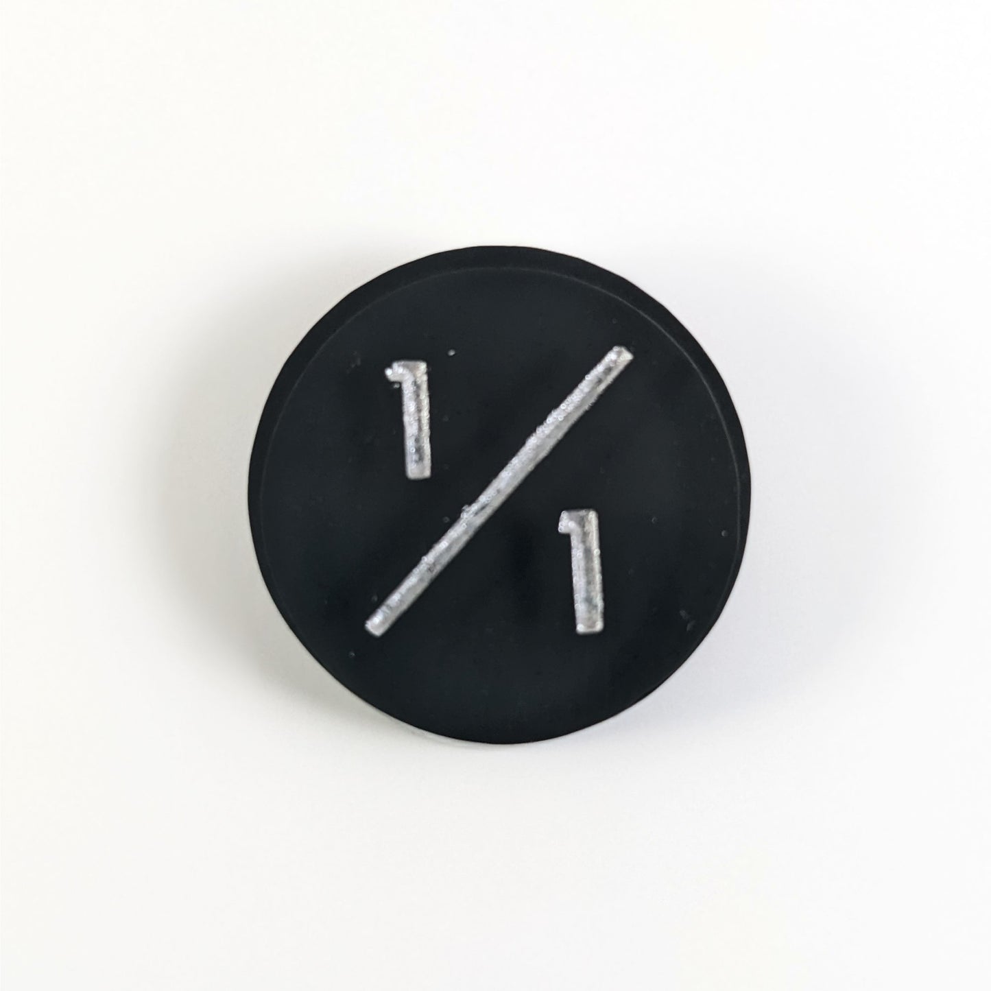 A top down photo of a black 1/1 token with silver numbers sits on a white background.
