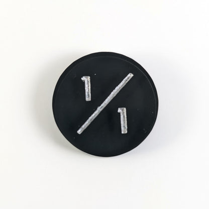 A top down photo of a black 1/1 token with silver numbers sits on a white background.
