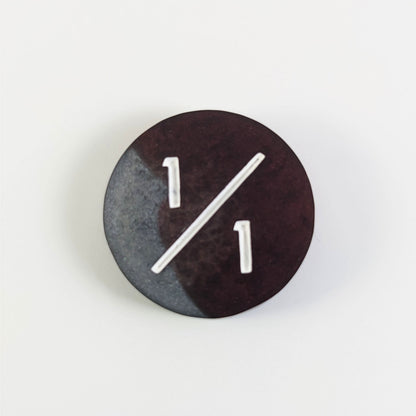 A top down photo of a silver and maroon 1/1 token with white numbers sits on a white background.