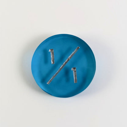 A top down photo of a blue 1/1 token with silver numbers sits on a white background.