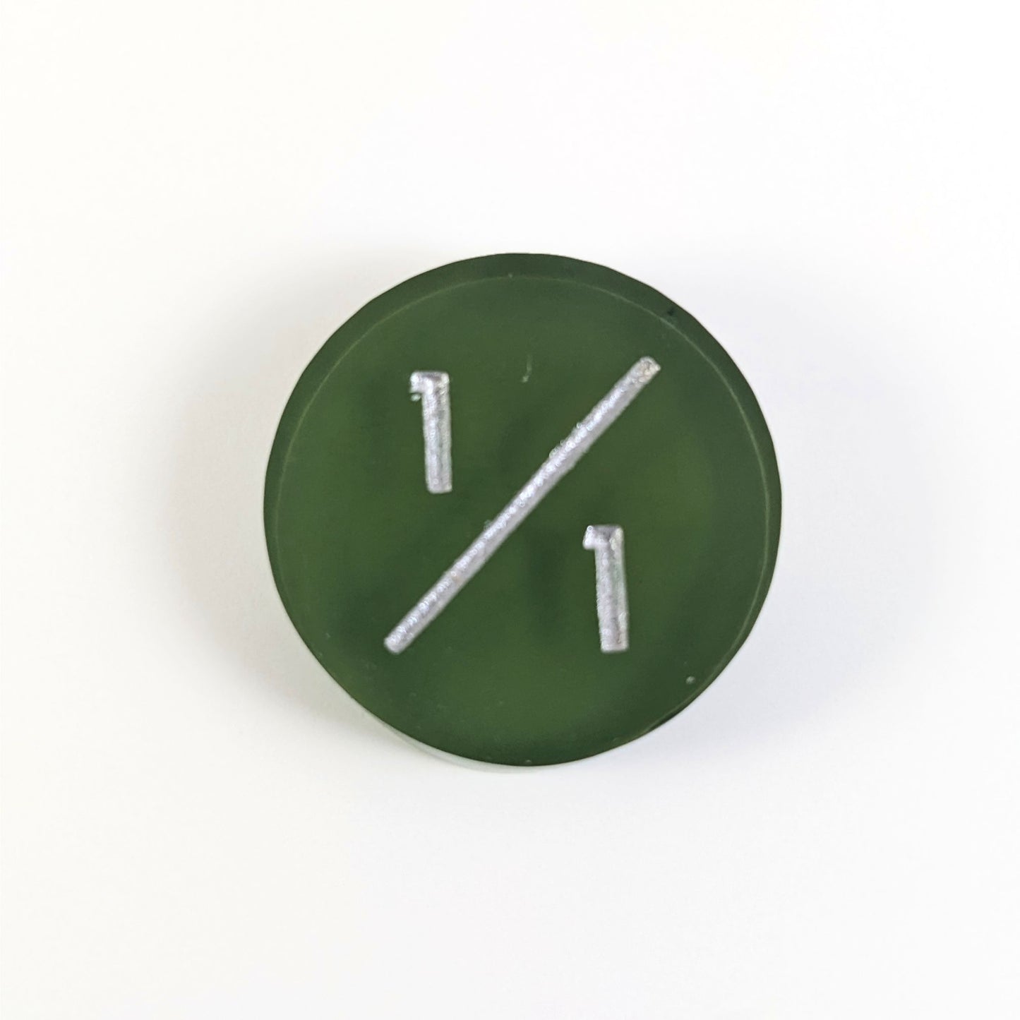 A top down photo of a dark green 1/1 token with silver numbers sits on a white background.