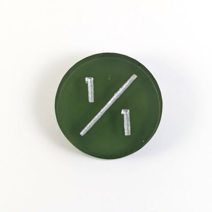 A top down photo of a dark green 1/1 token with silver numbers sits on a white background.