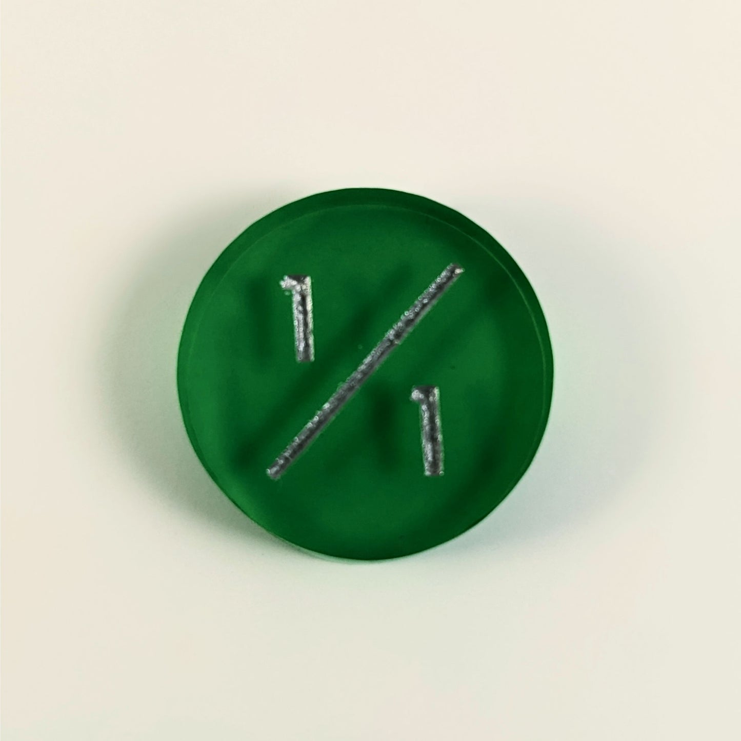 A top down photo of a green 1/1 token with silver numbers sits on a white background.