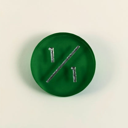 A top down photo of a green 1/1 token with silver numbers sits on a white background.