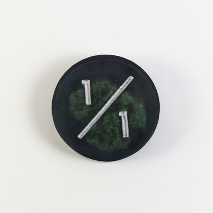 A top down photo of a green and black 1/1 token with silver numbers sits on a white background.