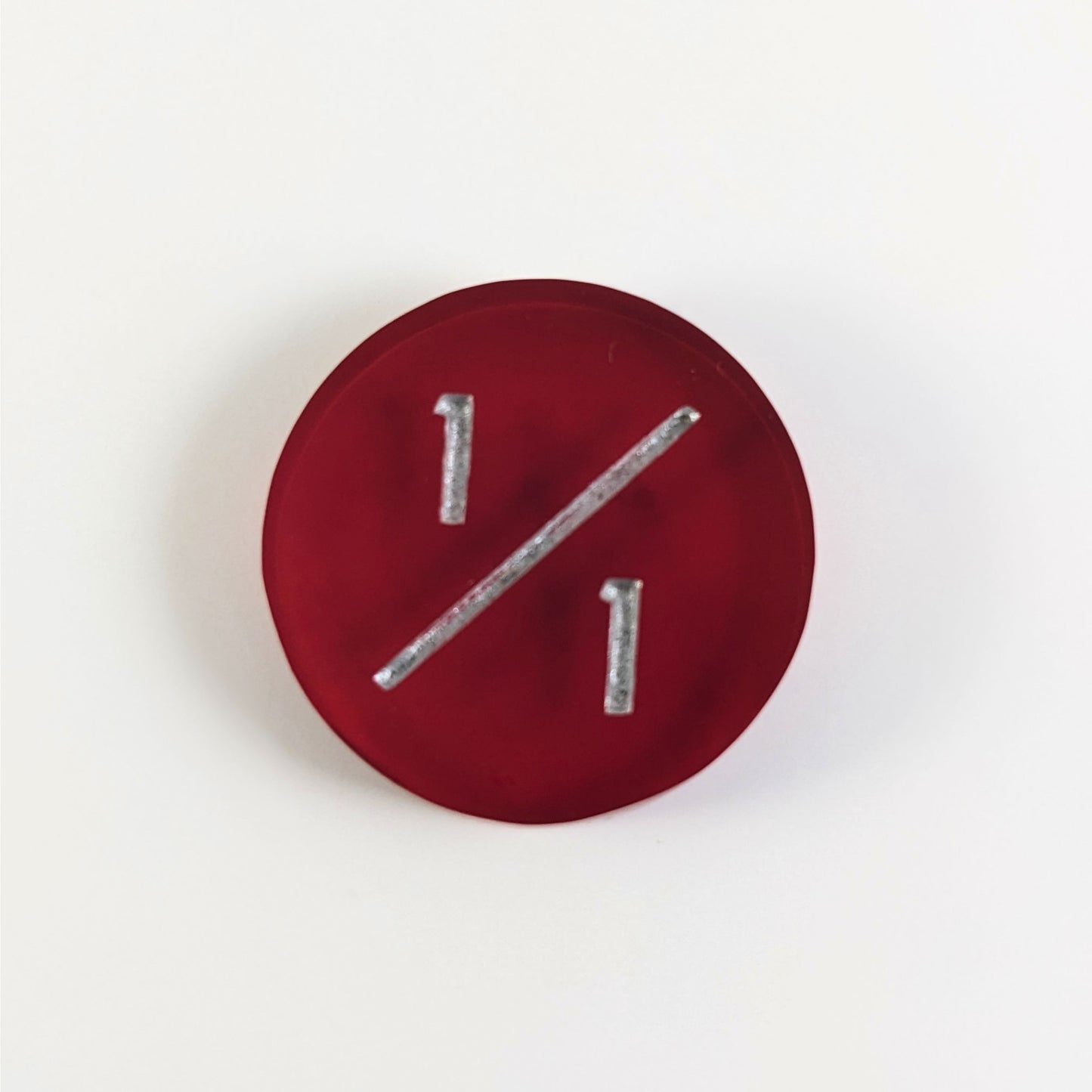 A top down photo of a red 1/1 token with silver numbers sits on a white background.