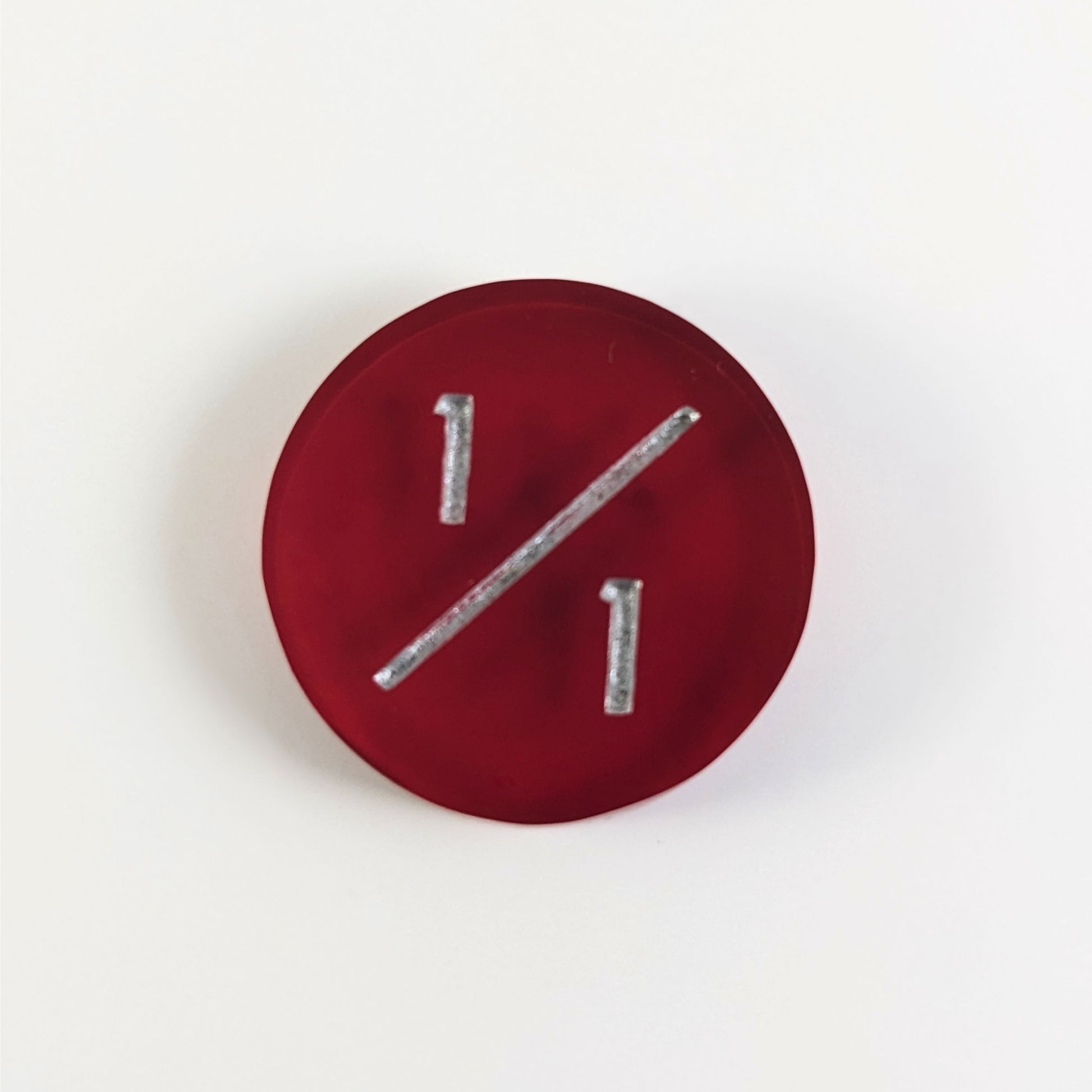 A top down photo of a red 1/1 token with silver numbers sits on a white background.