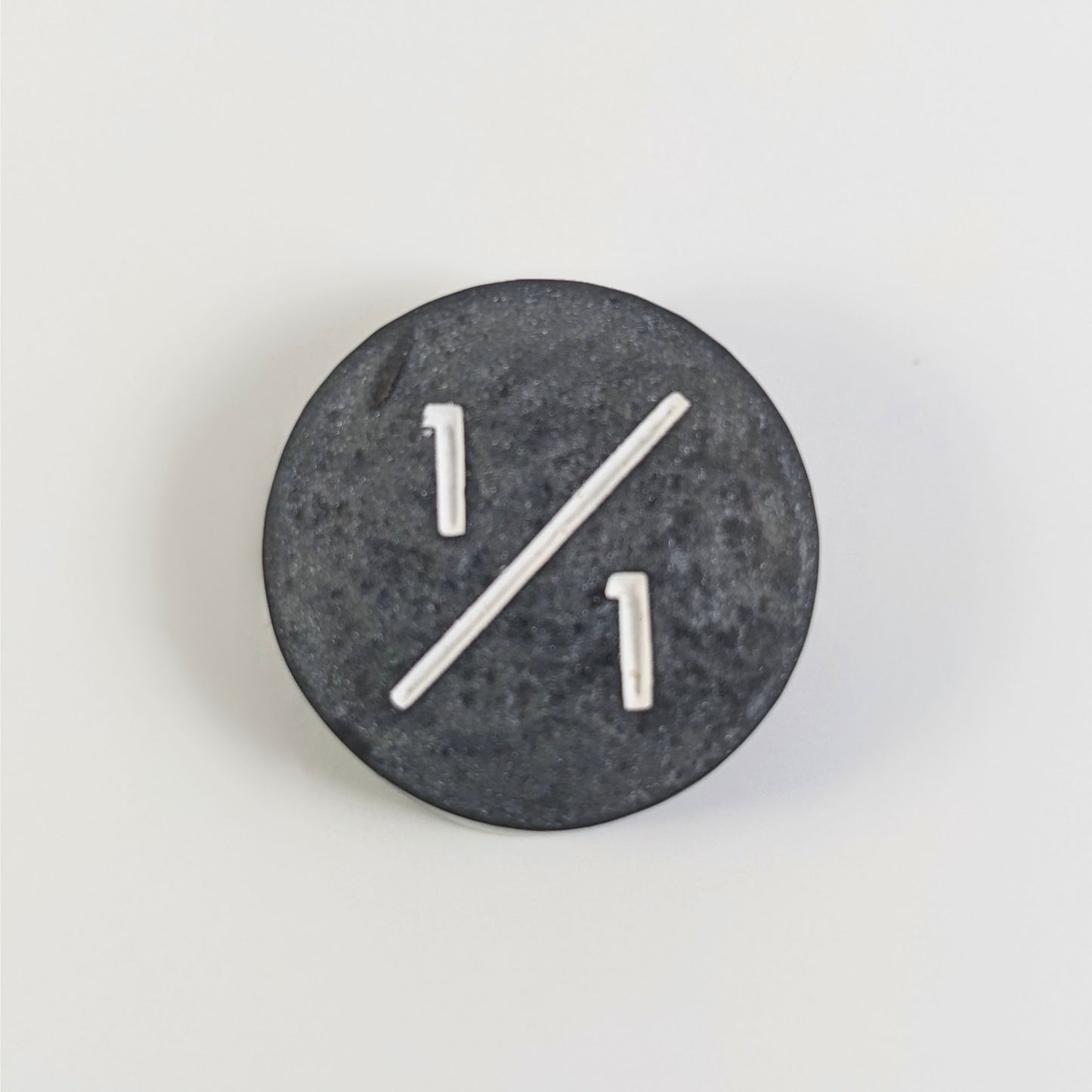 A top down photo of a silver 1/1 token with white numbers sits on a white background.