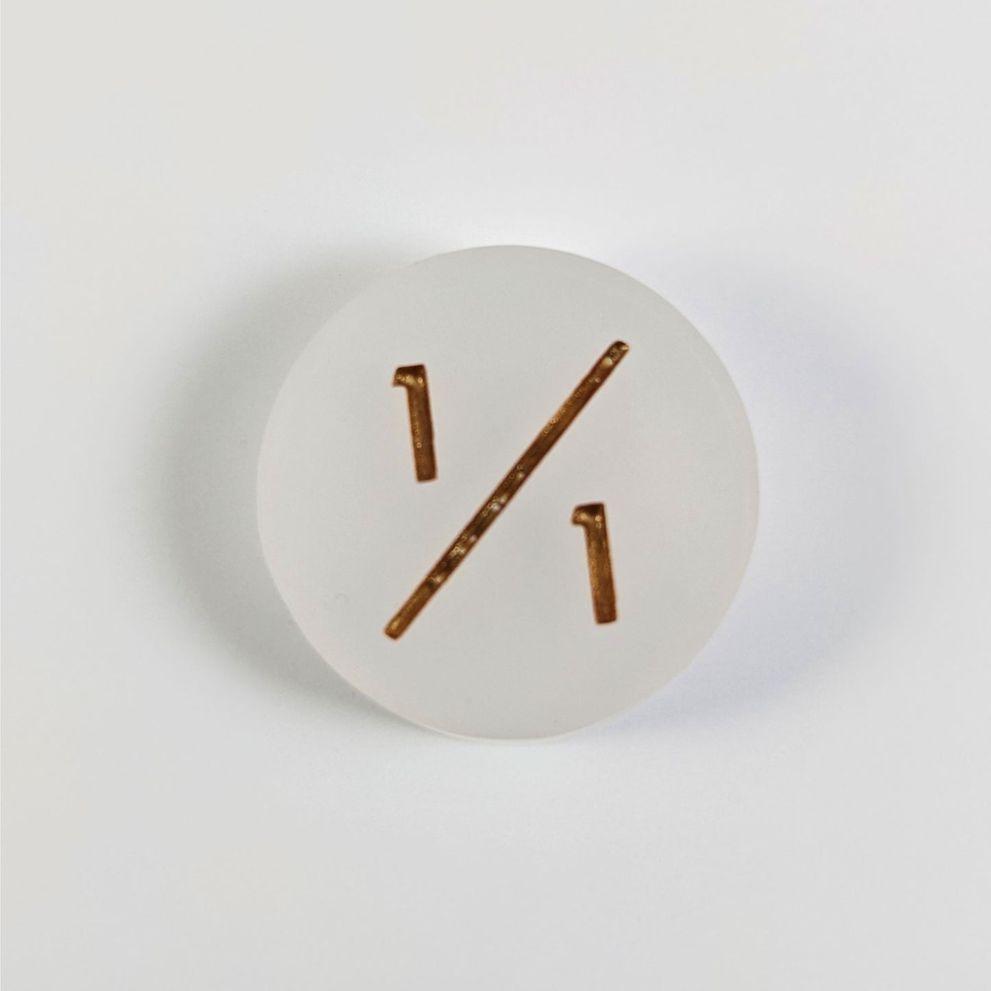 A top down photo of a white 1/1 token with gold numbers sits on a white background.