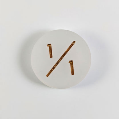 A top down photo of a white 1/1 token with gold numbers sits on a white background.