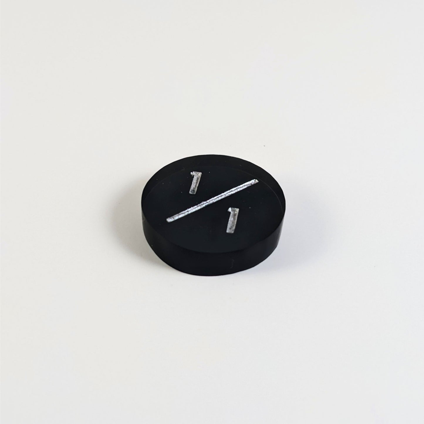A low angle photo of a black 1/1 token with silver numbers sits on a white background.