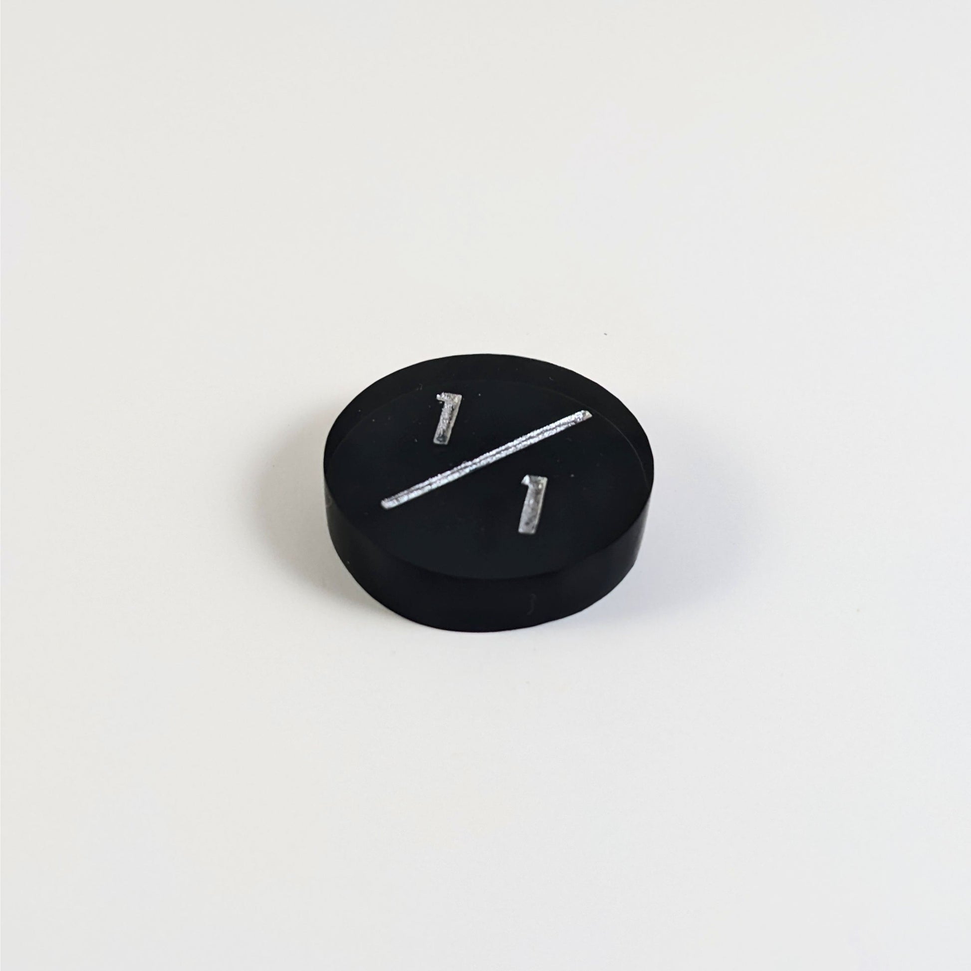 A low angle photo of a black 1/1 token with silver numbers sits on a white background.