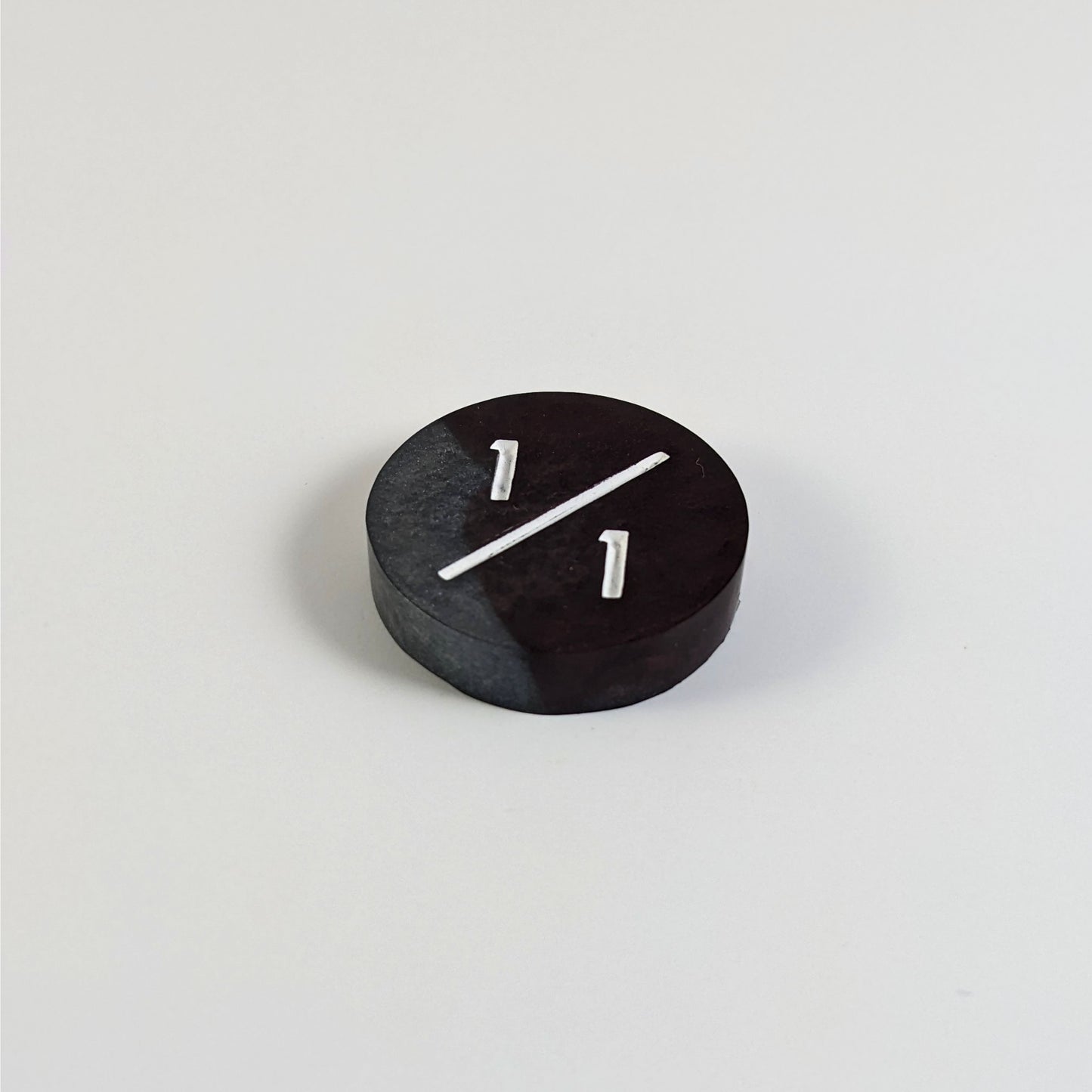A low angle photo of a silver and maroon 1/1 token with white numbers sits on a white background.