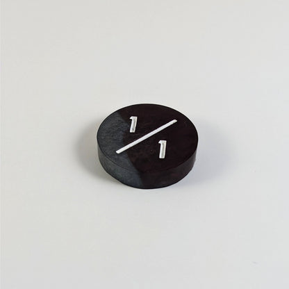 A low angle photo of a silver and maroon 1/1 token with white numbers sits on a white background.